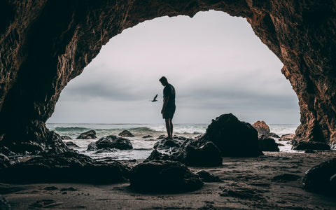 View from a cave looking out onto the ocean with a man stood in silhouette