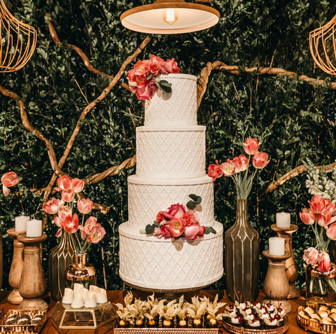 A decadent textured wedding cake sits  under amongst a luxurious spread of cakes, flowers and candles