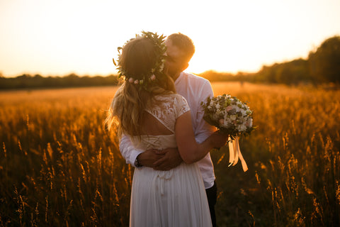 A bridal couple stood kissing in a cornfield with the sunsetting behind them.