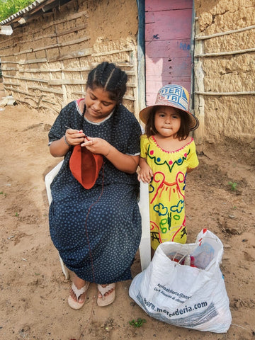 two young wayuu girls. one in black making a wayuu bag, the other one in yellow