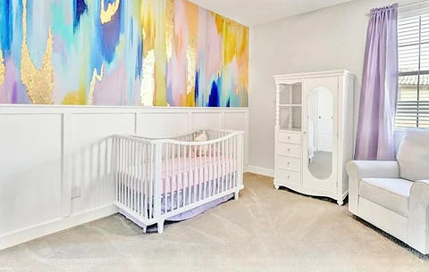 Nursery room with white decor and rainbow wallpaper mural design on the accent wall by the crib.