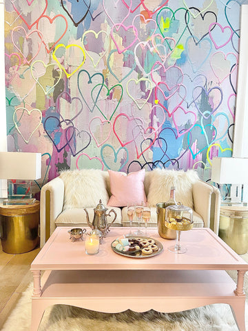 Heart themed wallpaper mural in a babe cave interior design project with white couch, pink coffee table and gold end tables.