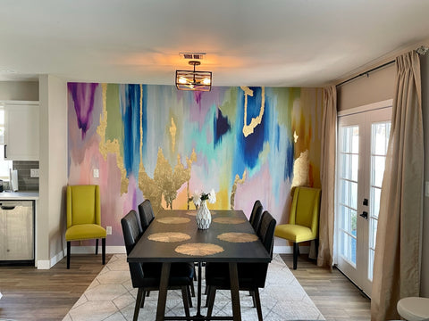 Modern dining room decor with a burst of color on accent wall using an abstract wallpaper mural filled with blues, pinks and gold tones.