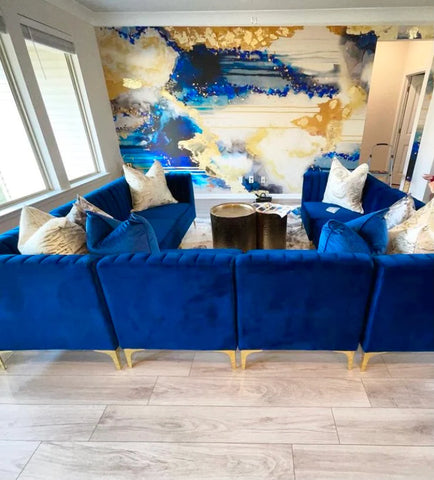 Blue themed interior design with blue suede sectional couch, white pillows and blue & gold abstract wallpaper mural from Vivian Ferne.