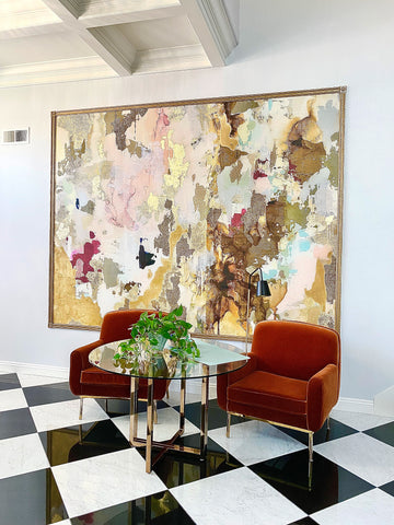 Luxury home with marble floor, recessed ceiling and colorful abstract framed artwork behind red velvet chairs.