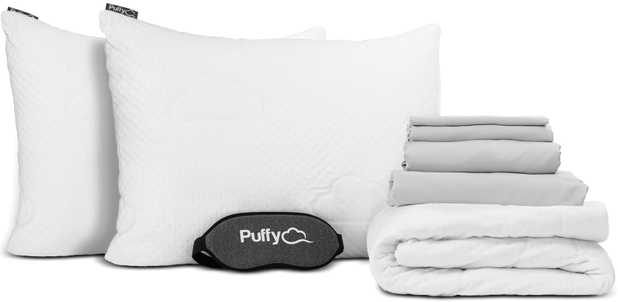 White folded mattress protector, two white pillows stacked, and a grey folded sheets set, part of the free Luxury Bedding Gifts bundle.