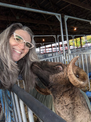 Natalia smiling while being nuzzled by a curly horned (not the technical term to be sure) sheep.