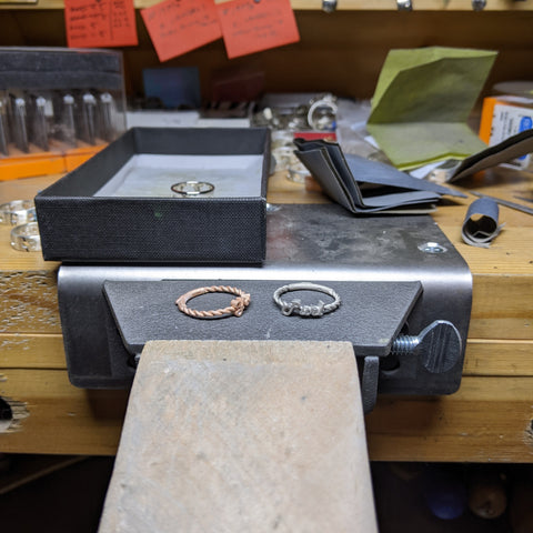 A rose gold ring next to a white gold ring on the bench pin of a jeweler's bench.