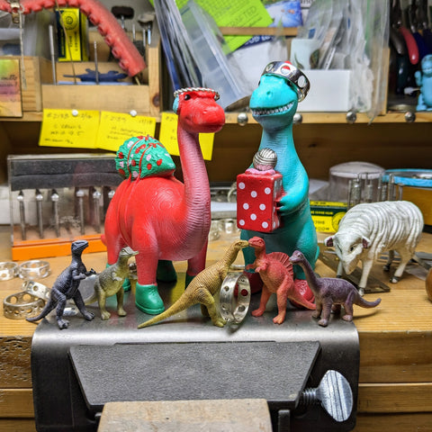 Plastic dinosaurs and unfinished jewelry on a busy workbench.