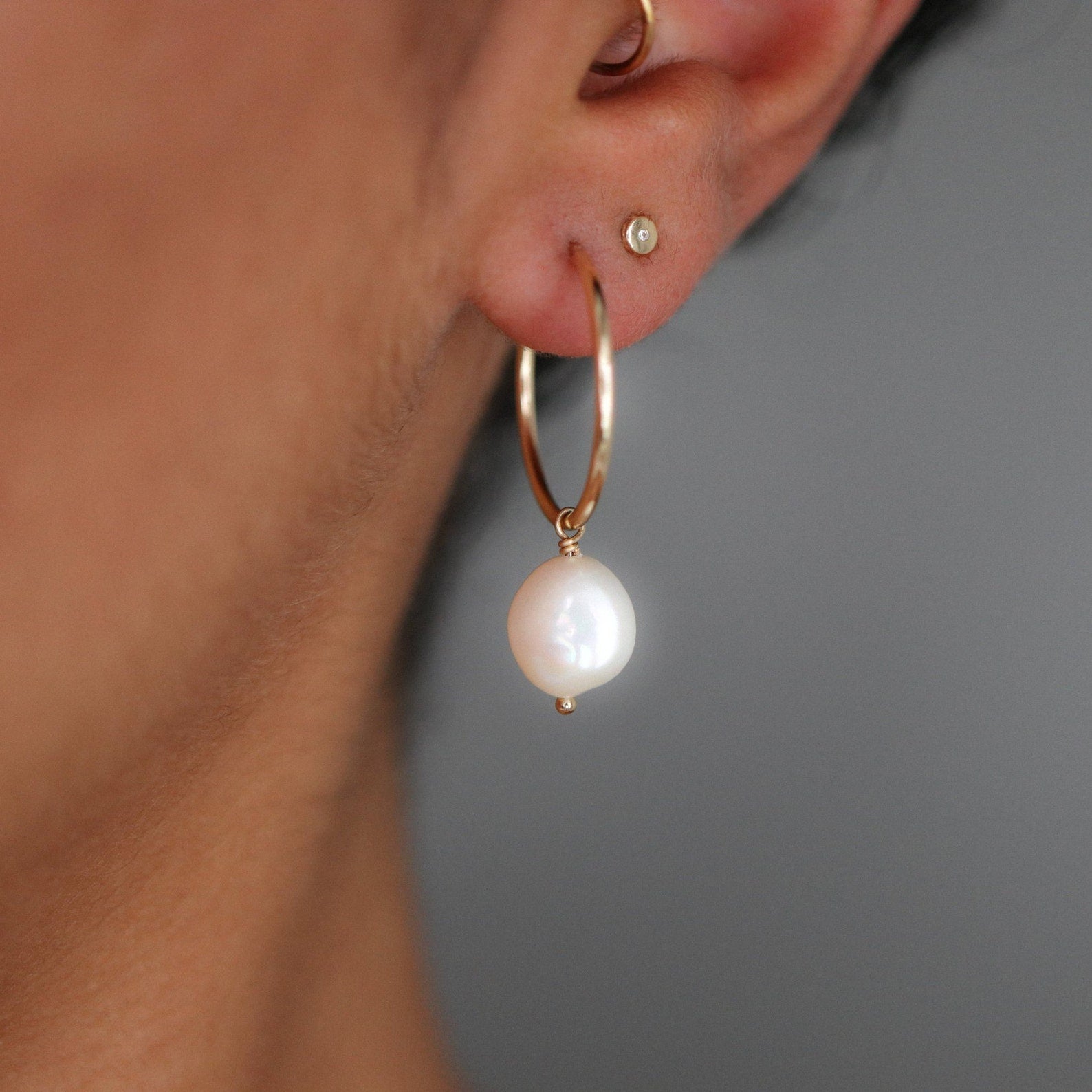 Gold hoop earring with white pearl drop hanging from it.