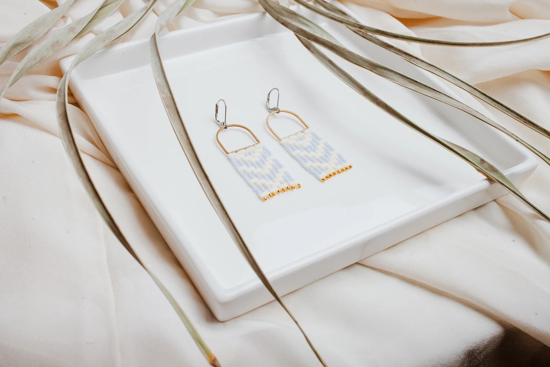 A pair of earrings made from blue, white and gold beads on a white stand.