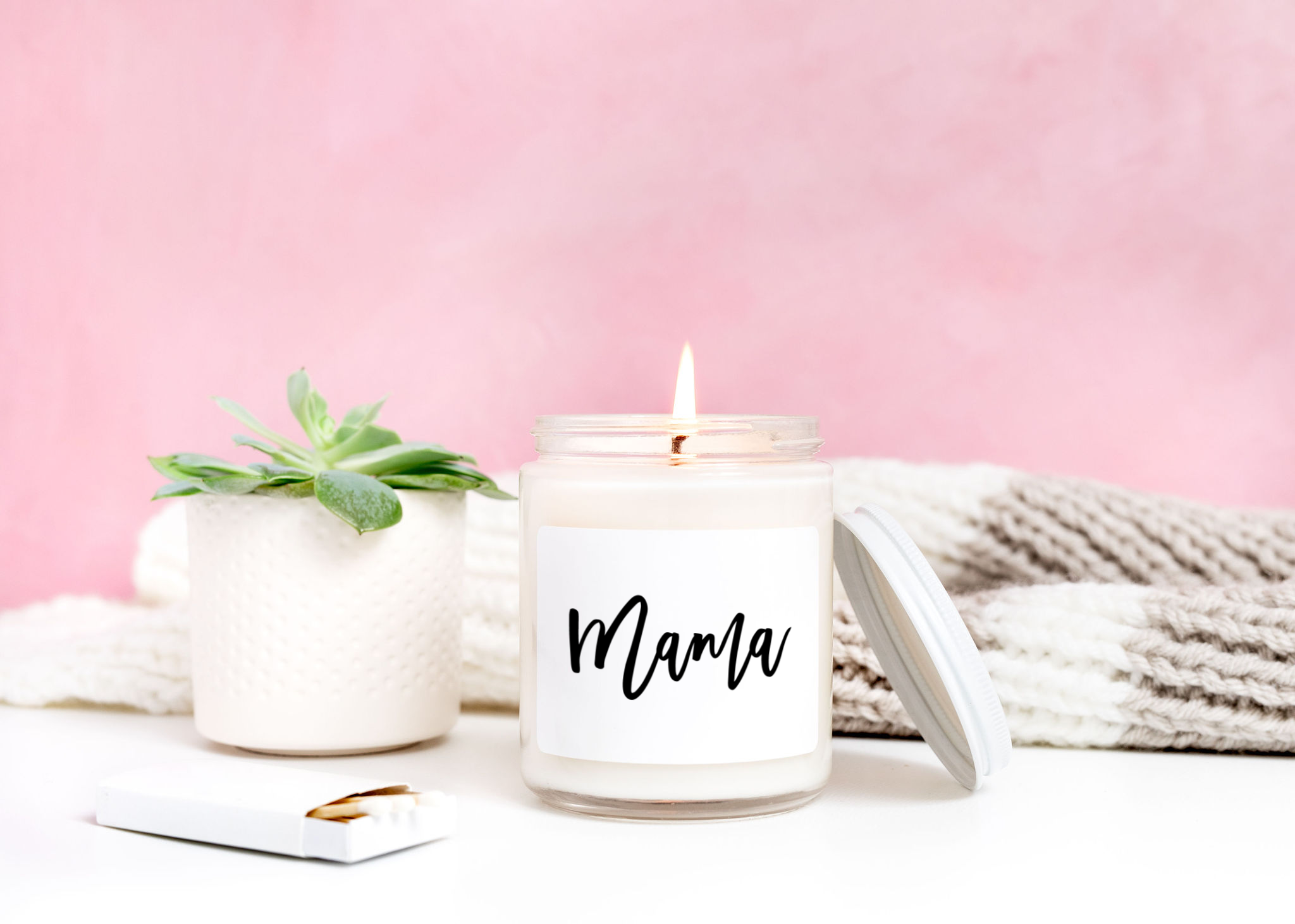 Mama candle lit in front of a pink background.