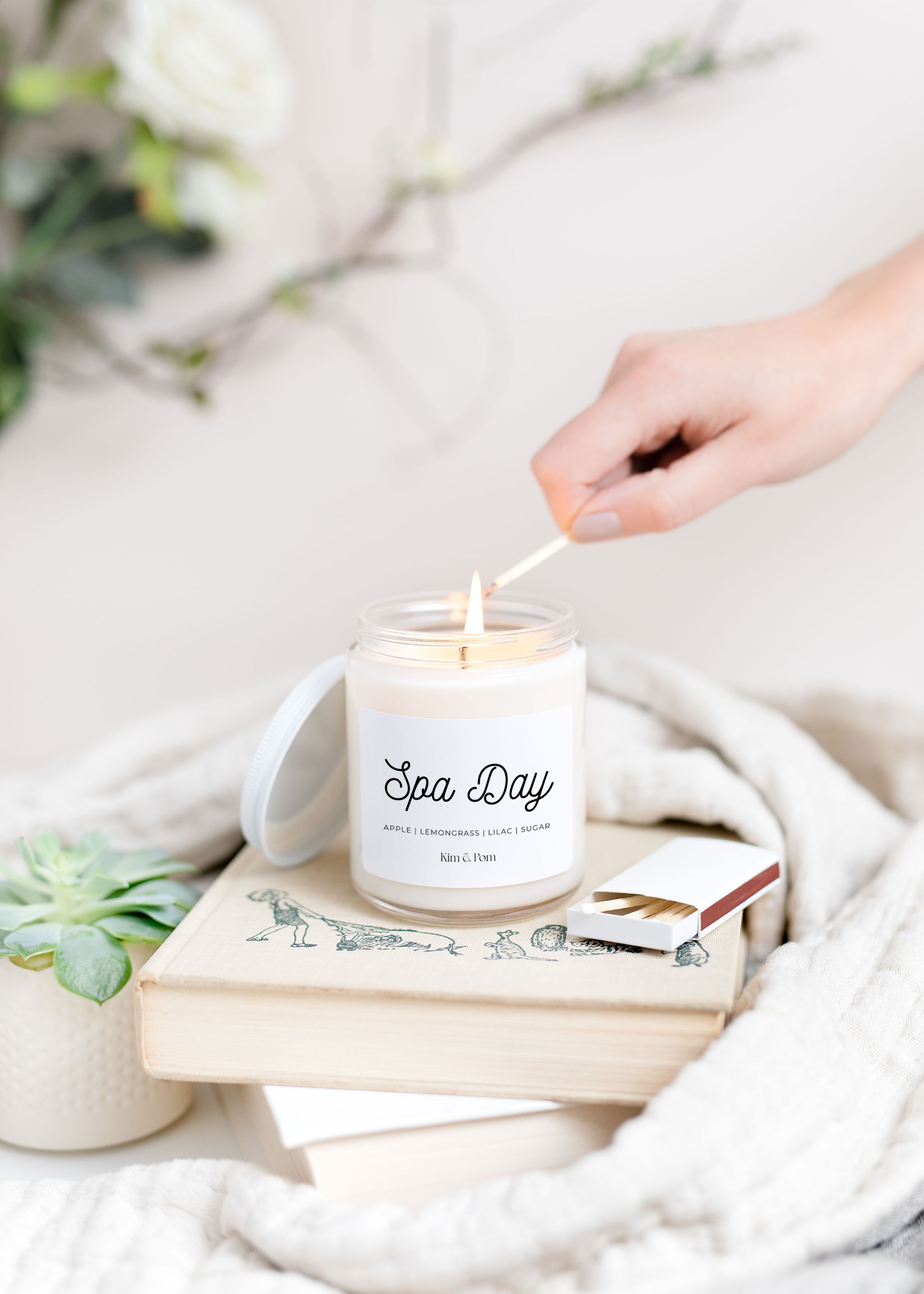 Spa Day candle being lit on top of a stack of books in front of a white background.