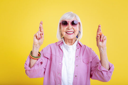 Senior woman in sunglasses smiling with fingers crossed