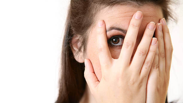 Woman hiding her face with her hands but peeping through her fingers