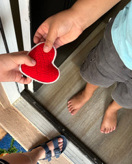 Image of one child handing a knit heart to another- FPK Red Knit Heart