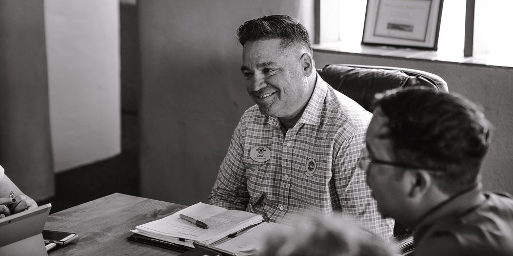 Two men sitting at the head of a conference table while talking with other people