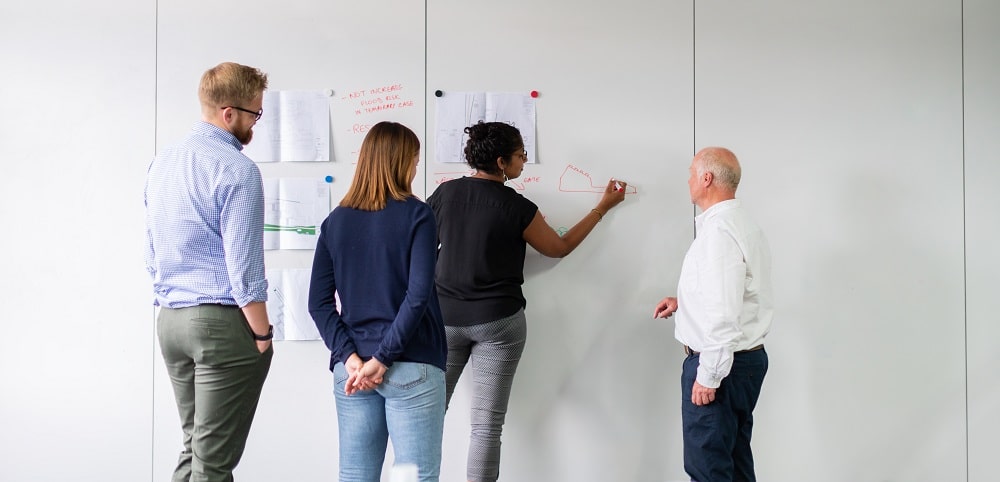 Employees writing notes on pieces of paper attached to the wall.