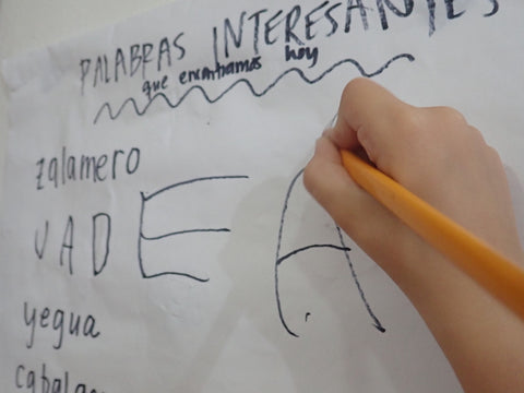 A child adds to a classroom chart called "Palabras Interesantes"