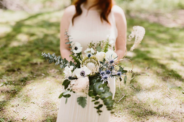 Bride holding bouquet featuring anemones, thistle, eucalyptus