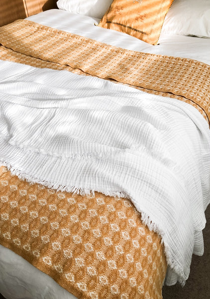mustard wool blanket and white textured cotton throw from sand and salt, covering a bed.