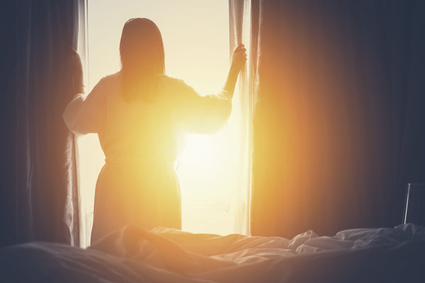 woman opening window curtains to sunshine Aromatics International