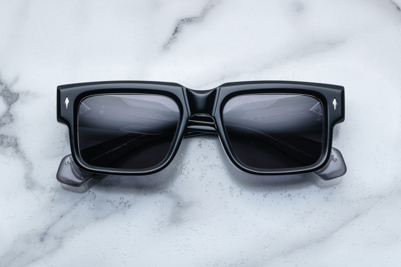 Thick square sunglasses frame lying folded on white marble surface