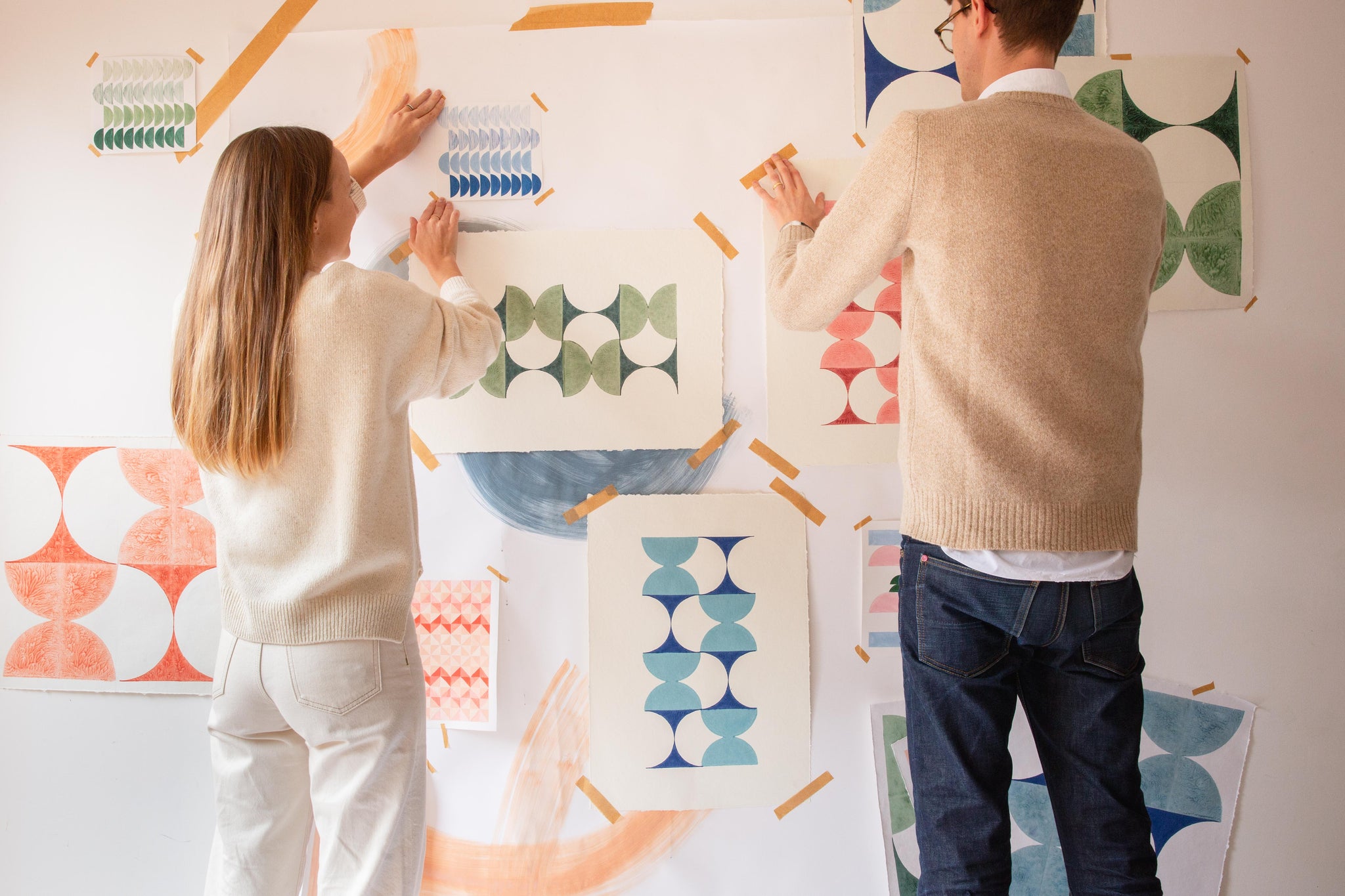 A woman and man sticking some art prints on a wall