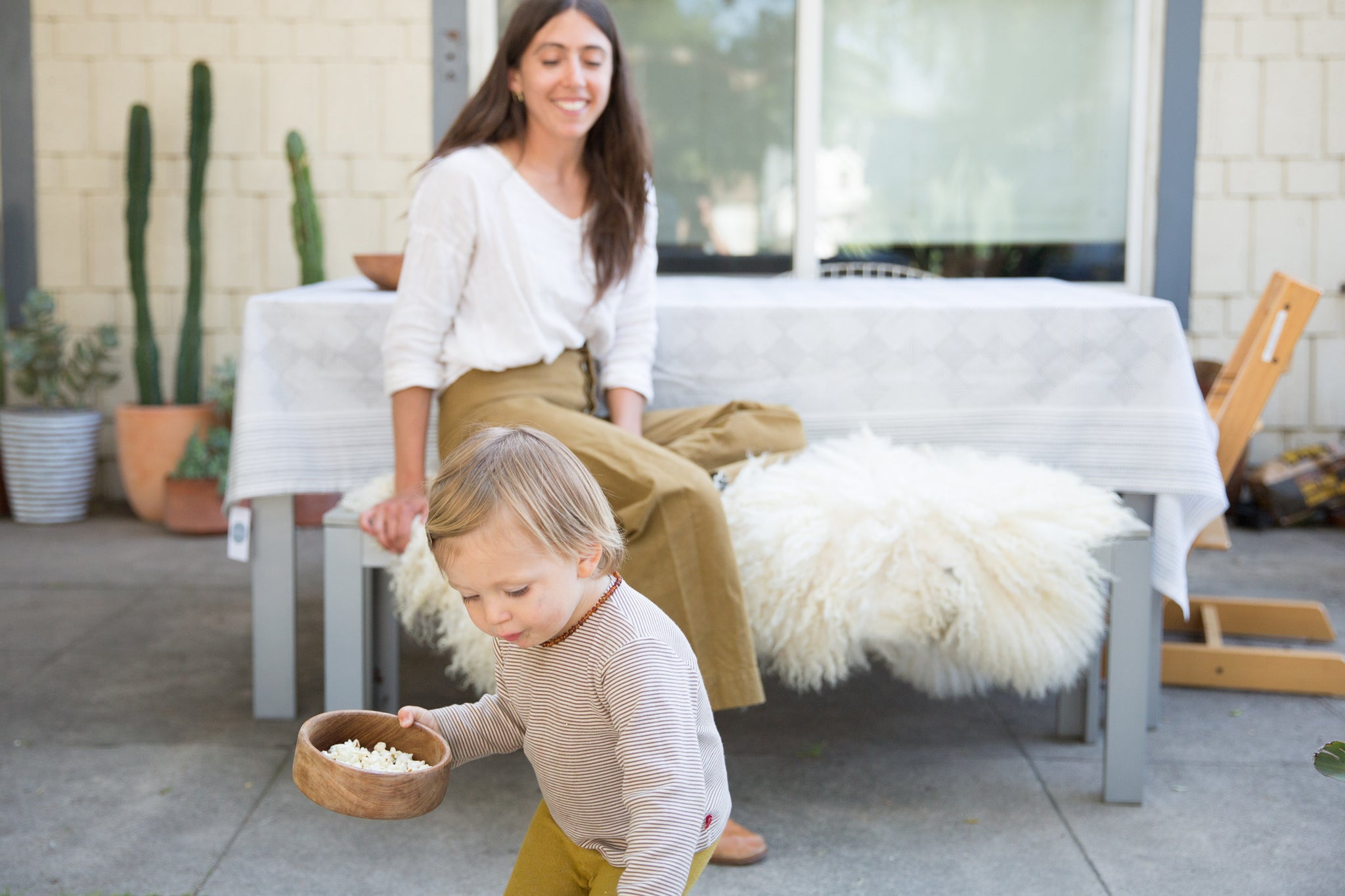 Dotter owner, Annika Huston, sitting beside outdoor table with table cloth; toddler son standing in foreground