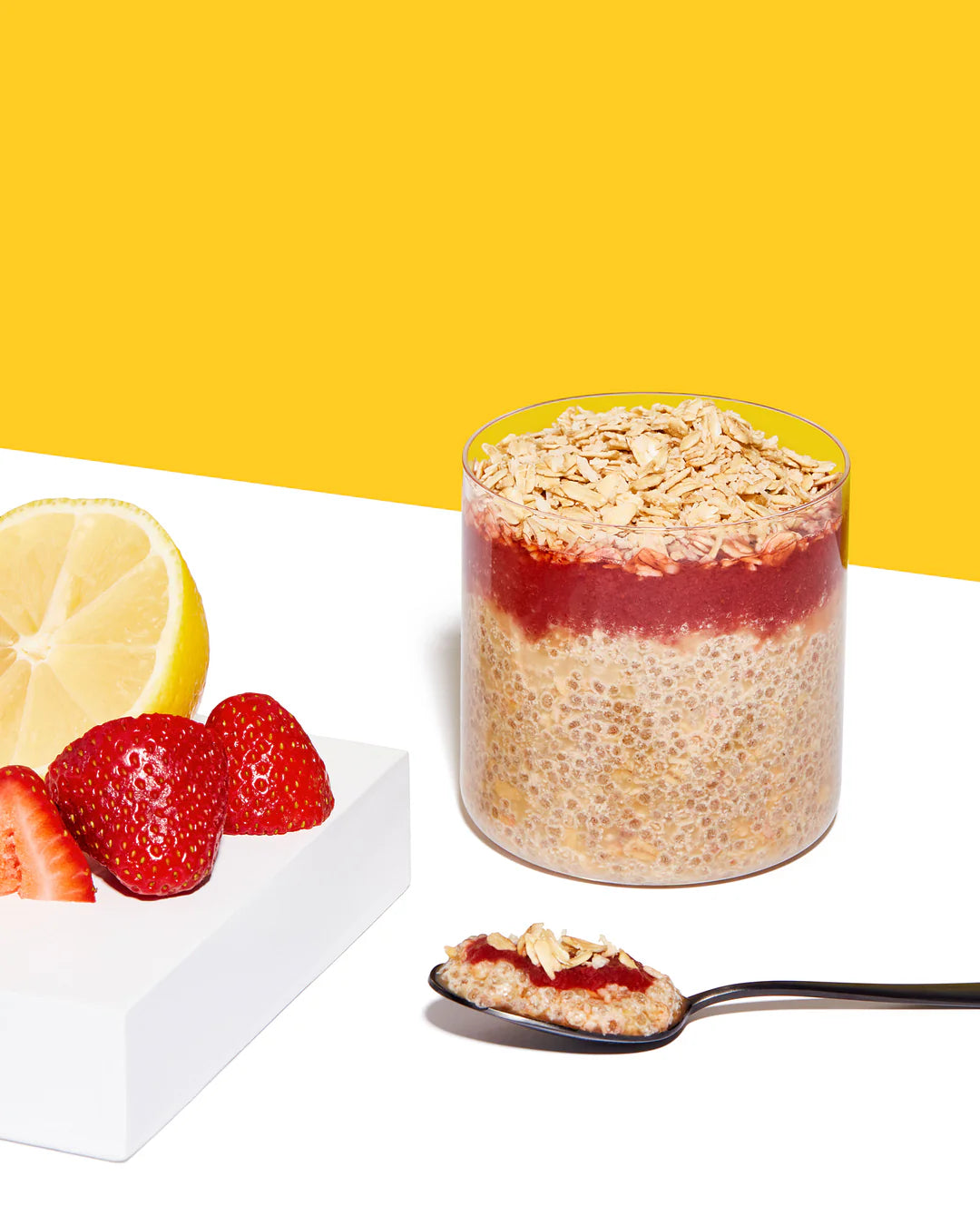 Layered chia pudding with strawberry puree and oats, accompanied by fresh strawberries and a lemon slice.