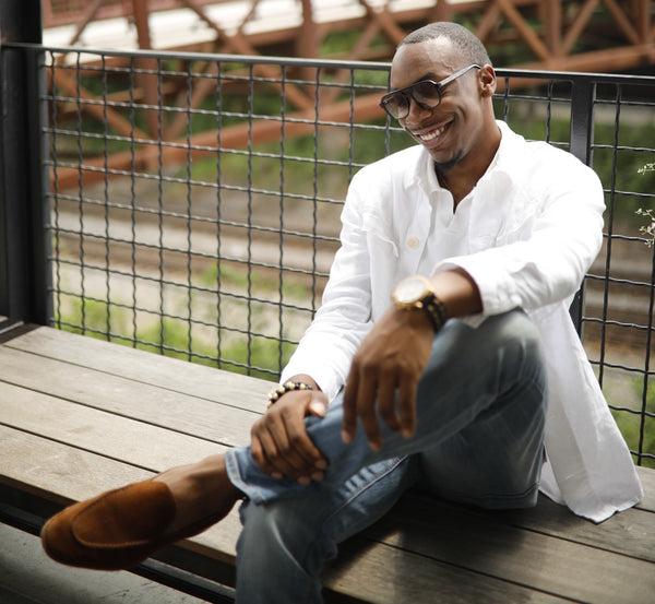 black man wearing brown suede loafers and white button down shirt while sitting on wooden bench
