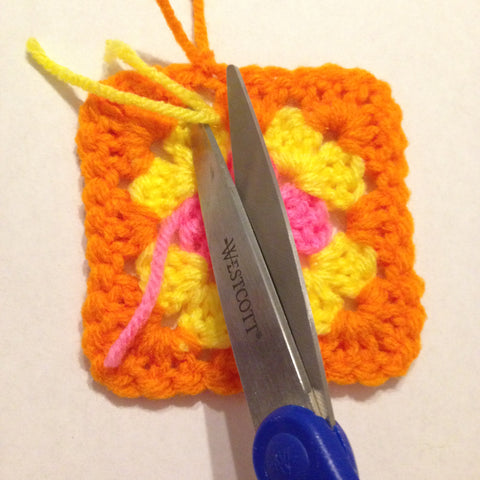 trimming the tails of yarn on a granny square