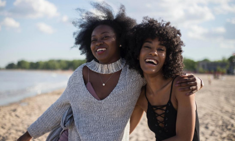 Two black women hugging and laughing in the sun