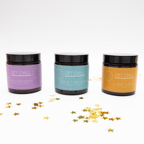 Set of three candles in amber jars with purple, teal and yellow labels