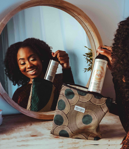 Girl with Afro looking in mirror and holding Afrocenchix bottle