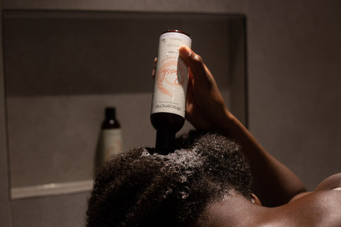 Back view of a woman applying Afrocenchix shampoo in the shower