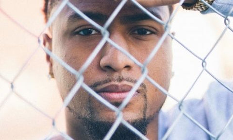 black man with beard standing in front of a metal fence