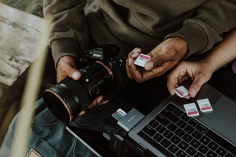 Close up of hands holding a camera, SD cards and a laptop