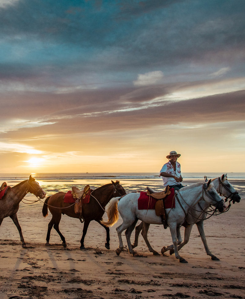 Caballero cowboy riding his horses on the beach during sunset in Costa Rica. Photographed by Kristen M. Brown, Samba to the Sea for The Sunset Shop.