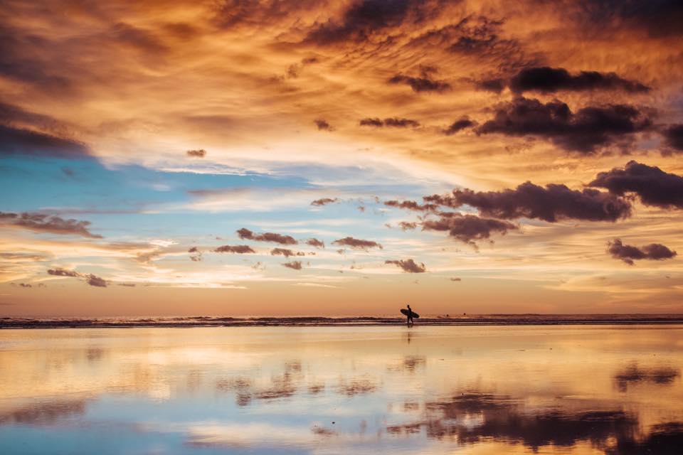 Surfer walking on the beach during a golden sunset in Costa Rica. Photographed by Kristen M. Brown, Samba to the Sea for The Sunset Shop.