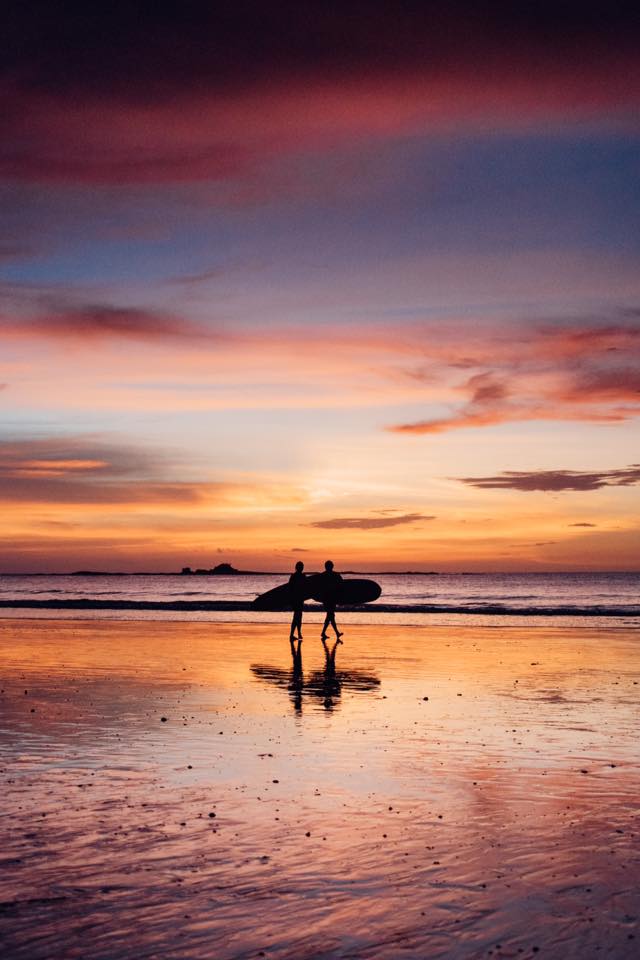Surfers walking on the beach in Costa Rica at sunset. Photographed by Kristen M. Brown, Samba to the Sea for The Sunset Shop.