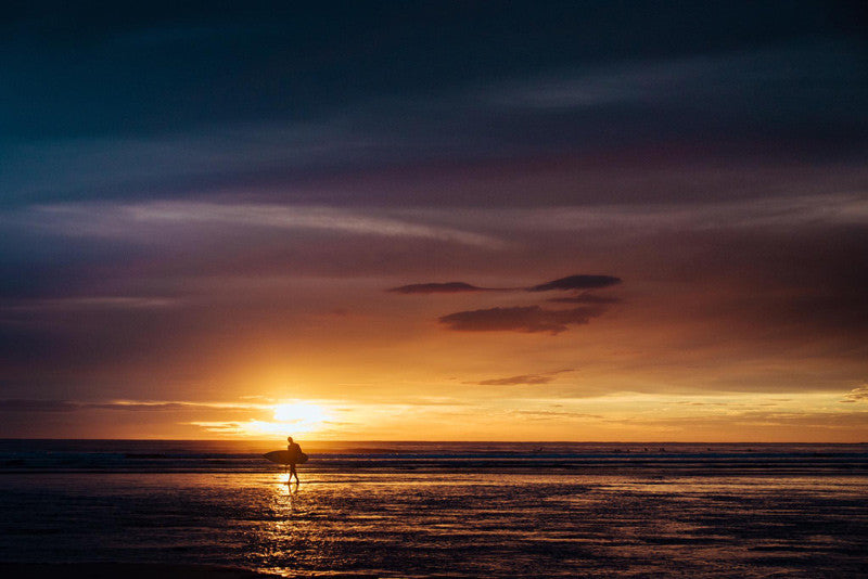 Surfer walking on the beach during sunset in Tamarindo Costa Rica. Photographed by Kristen M. Brown, Samba to the Sea for The Sunset Shop.