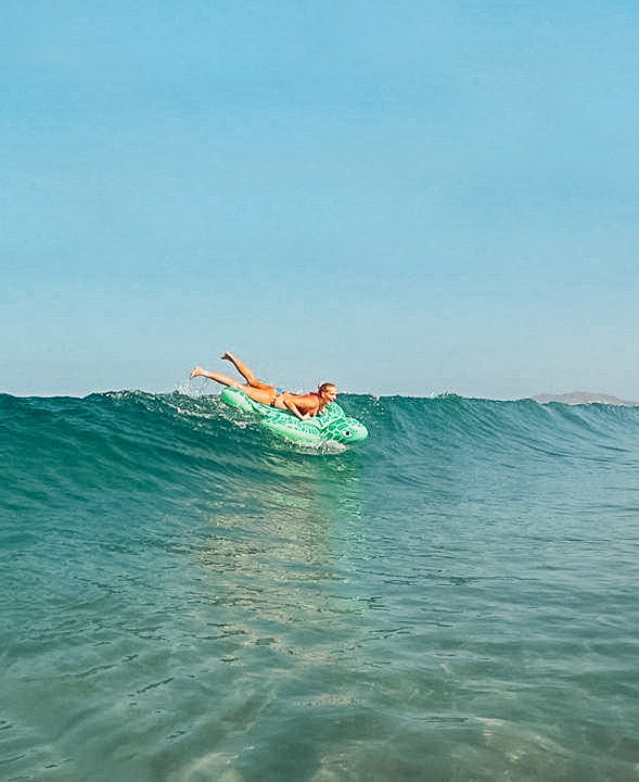 Surfer girl riding an inflatable sea turtle in the Pacific Ocean in Costa Rica. Photographed by Kristen M. Brown, Samba to the Sea for The Sunset Shop.