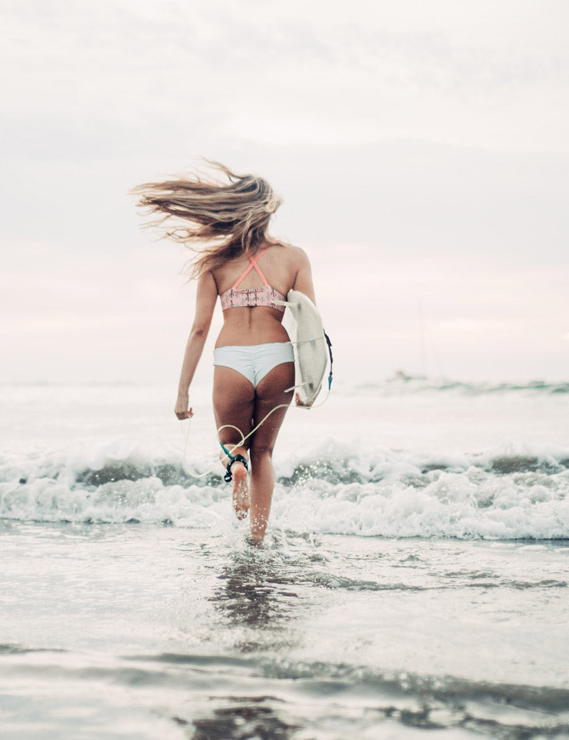 Female surfer running into the ocean in Tamarindo Costa Rica. Photographed by Kristen M. Brown, Samba to the Sea for The Sunset Shop.
