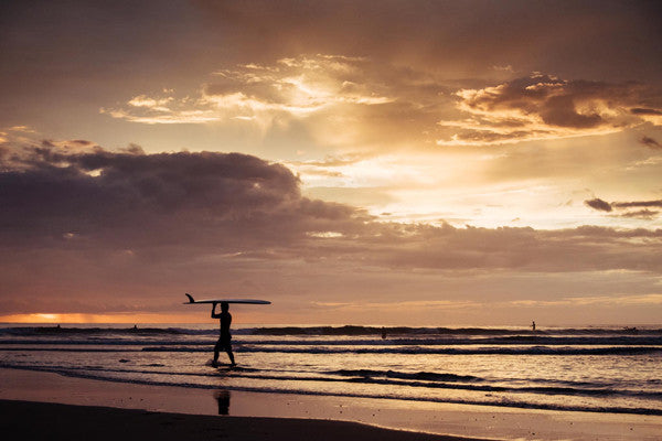 Surfer walking on the beach during sunset in Playa Tamarindo, Costa Rica. Photographed by Kristen M. Brown, Samba to the Sea at The Sunset Shop.