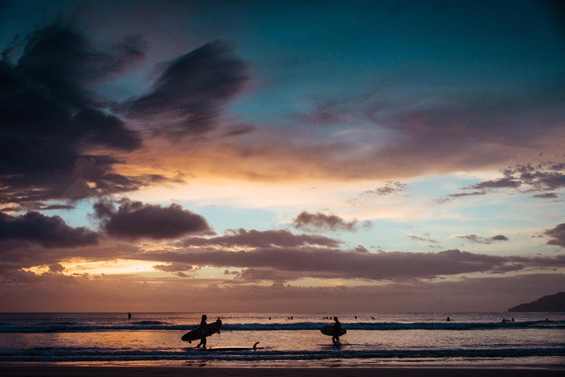 Female surfers walking out of the ocean after a sunset surf in Tamarindo Costa. Photographed by Kristen M. Brown, Samba to the Sea for The Sunset Shop.