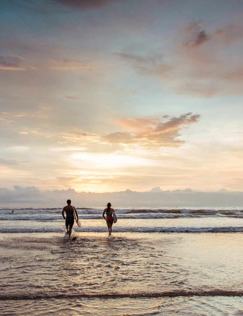Surfers running into the ocean in Costa Rica at sunset. Photographed by Kristen M. Brown, Samba to the Sea for The Sunset Shop.