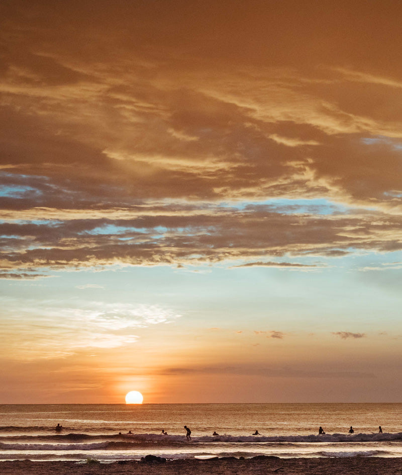 Surfers in the ocean in Tamarindo Costa Rica as the sun passes over the horizon. Photographed by Kristen M. Brown, Samba to the Sea for The Sunset Shop.