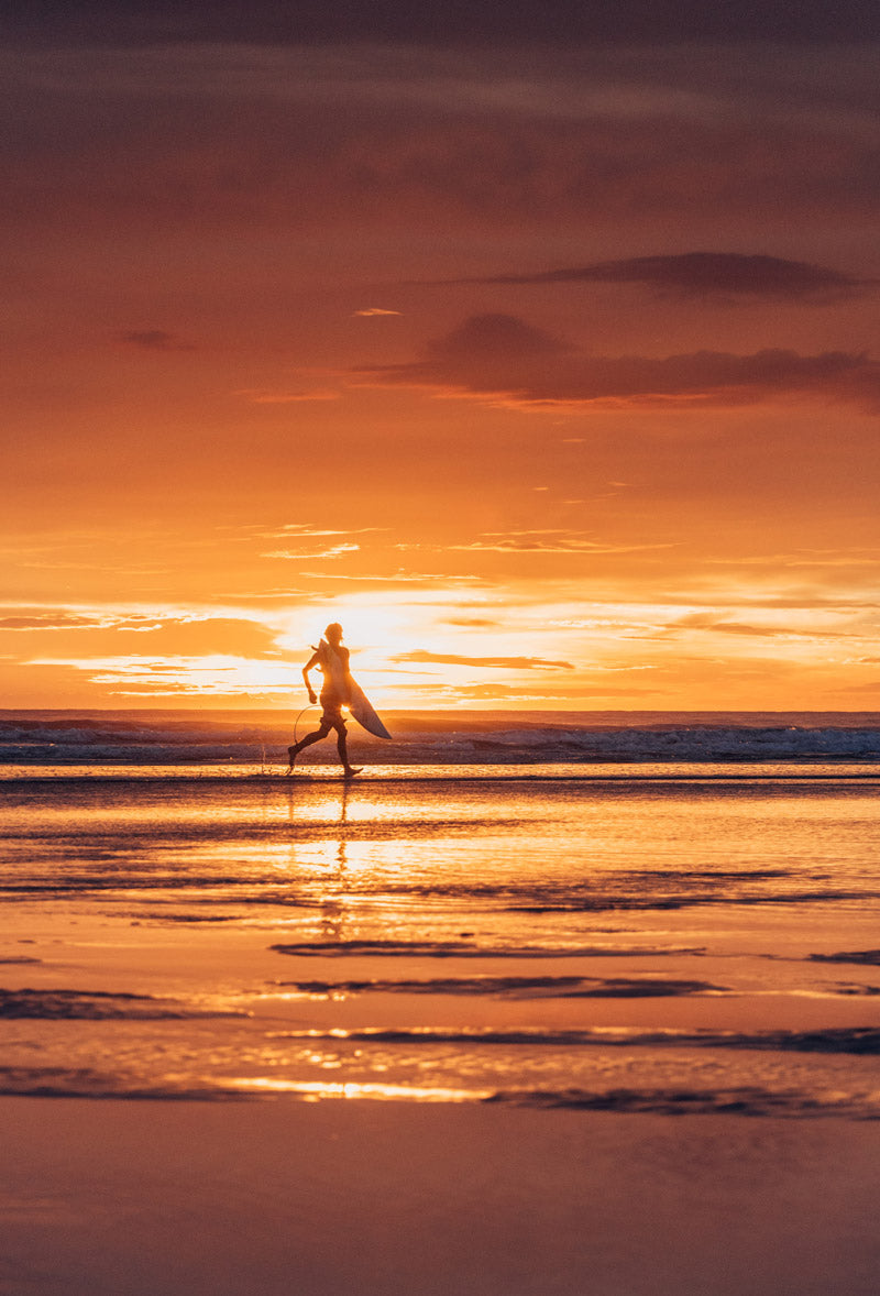 Surfer running on the beach in Tamarindo Costa Rica during sunset. Photographed by Kristen M. Brown, Samba to the Sea for The Sunset Shop.