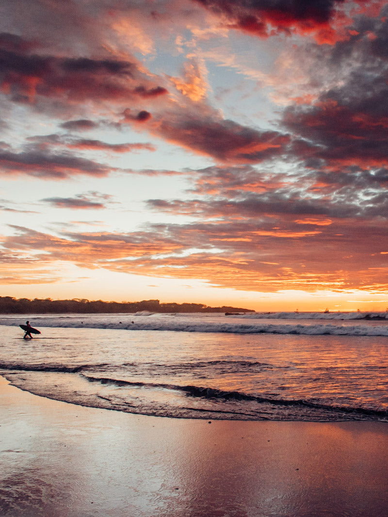 Surfer walking on the beach during sunset in Tamarindo Costa Rica. Sunset art pictures photographed by Kristen M. Brown, Samba to the Sea for The Sunset Shop.